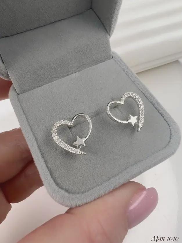 Heart-shaped earrings with star details in a gray jewelry box held by a hand.