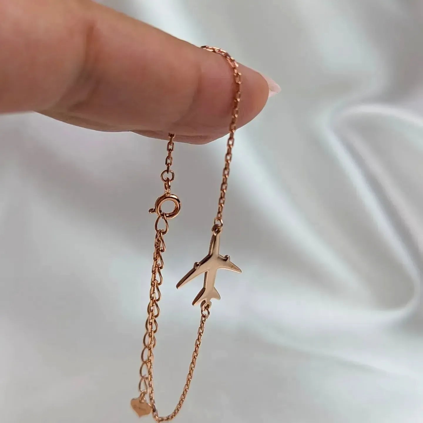 Rose gold airplane-shaped pendant on a chain held by a hand against a white background