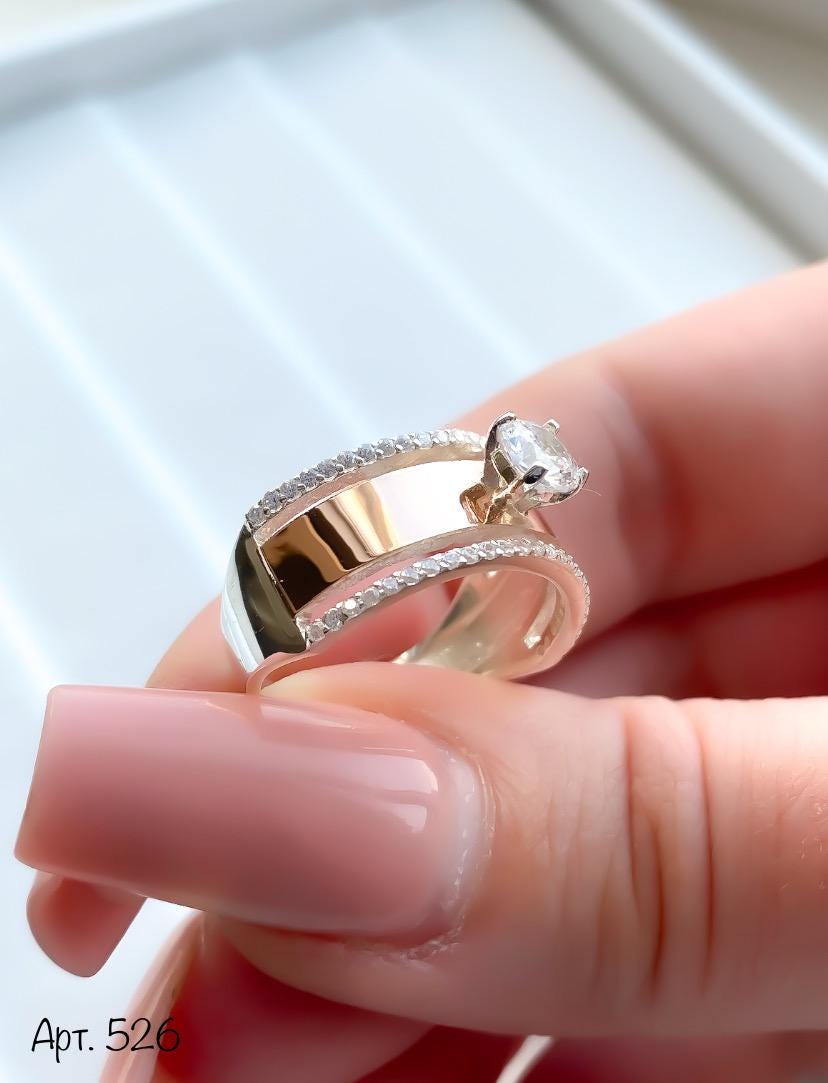 Close-up of a hand holding two gold rings with diamond accents.