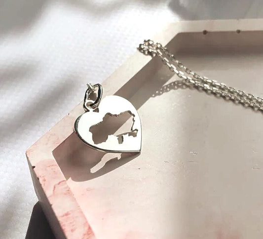 Silver heart-shaped necklace with a map design on a light pink surface