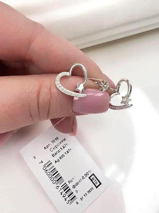Silver heart-shaped earrings held by a hand with a white background
