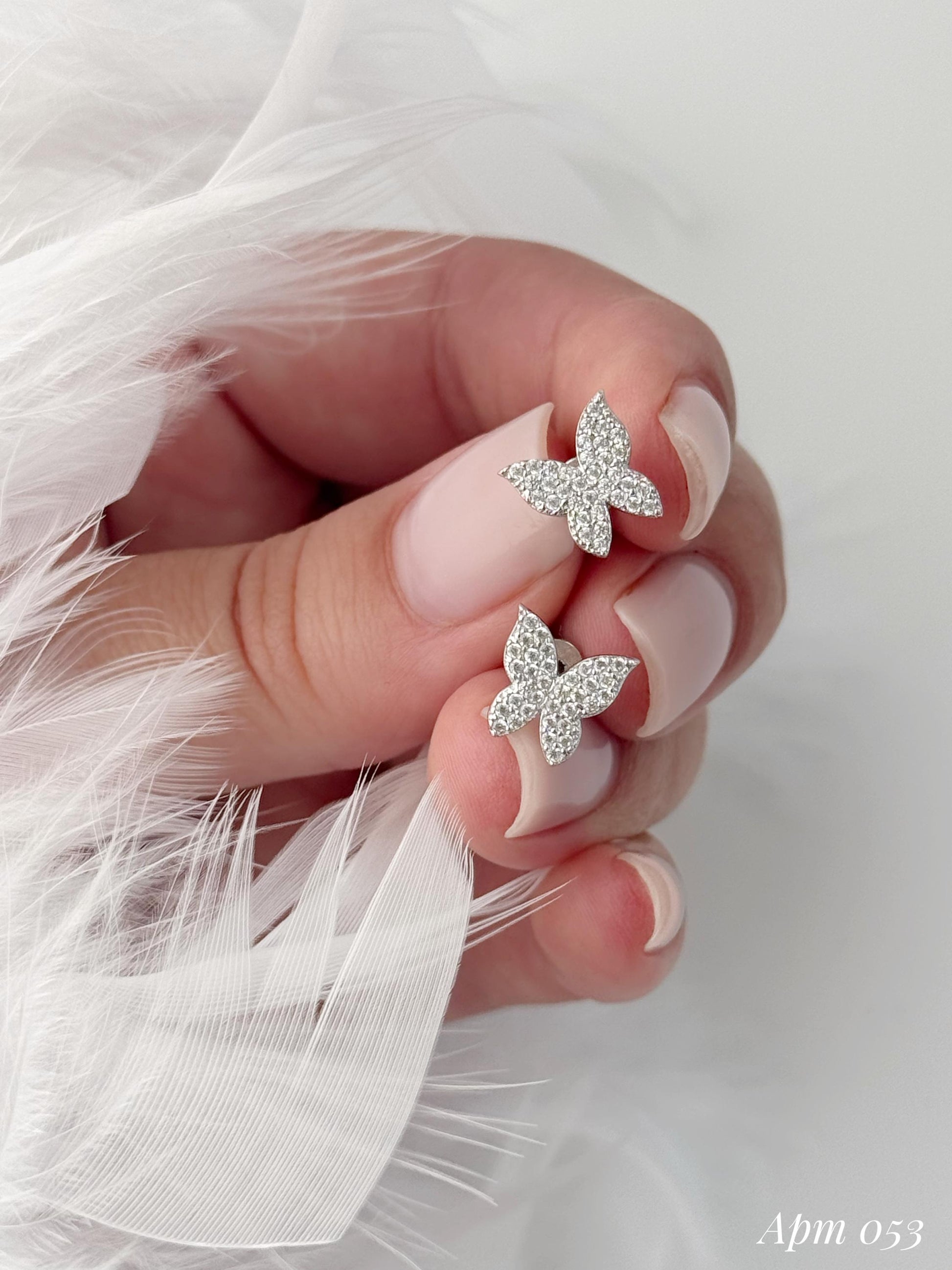 Butterfly-shaped earrings on a hand with white feathered background
