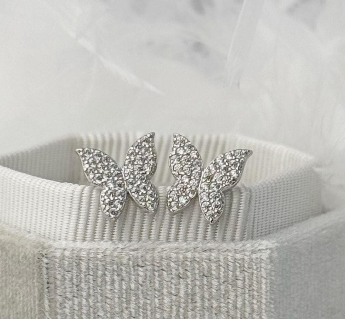 Butterfly-shaped earrings with rhinestones on a textured surface