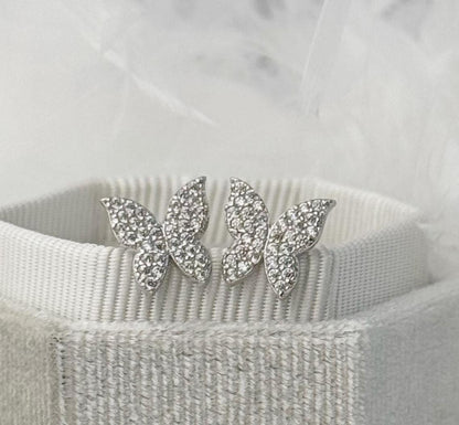 Butterfly-shaped earrings with rhinestones on a textured surface