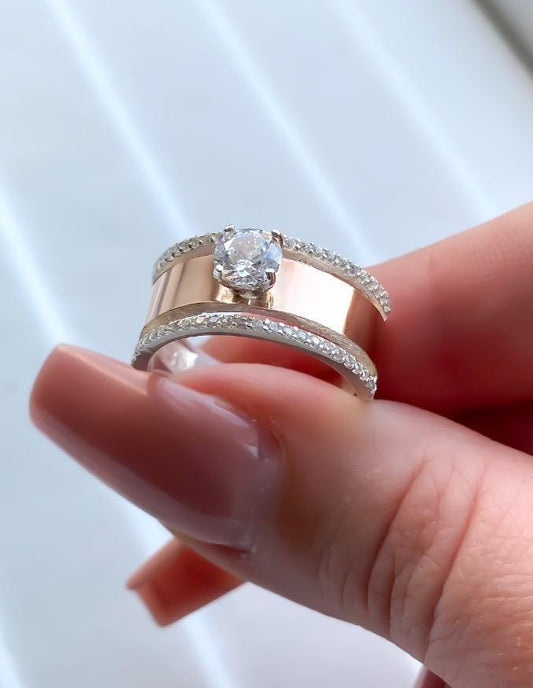 Rose gold ring with a diamond held in a hand against a white background