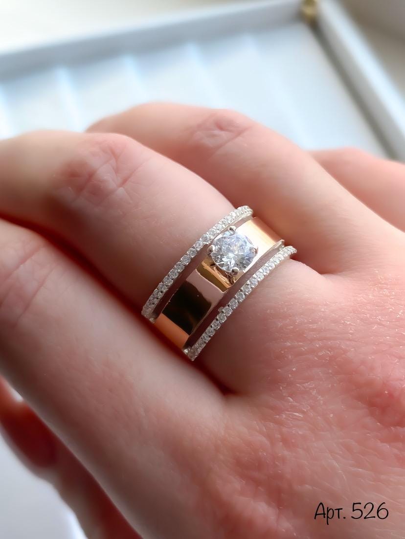 Rose gold ring with diamond on a hand against a neutral background